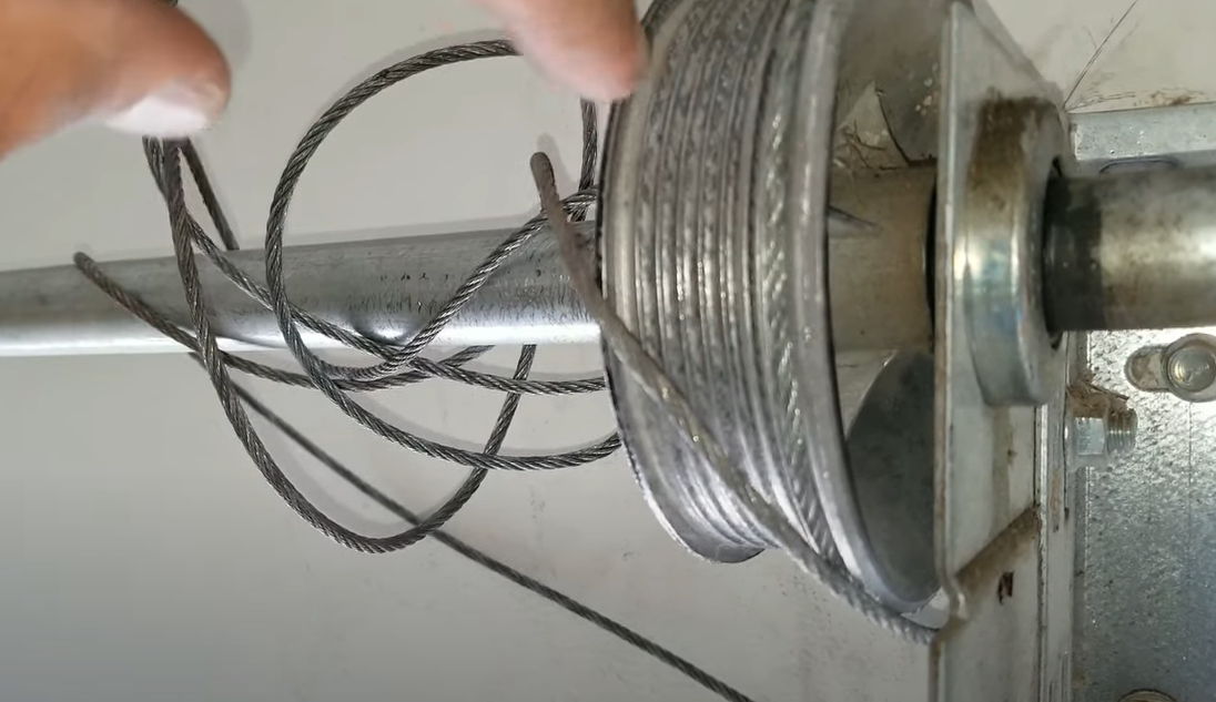 Technician performing a garage door cable repair with close-up focus on the hands and tools in action.